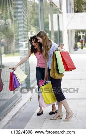 Stock Photo - Two women with shopping bags looking at shop window. Fotosearch