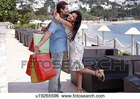 Woman embracing man holding shopping bags View Large Photo Image Stock Photograph - Woman embracing man holding shopping bags. Fotosearch