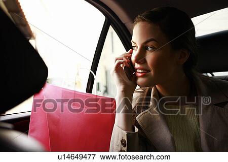 Stock Photo - Woman on the cell phone with shopping bags in a taxi. Fotosearch