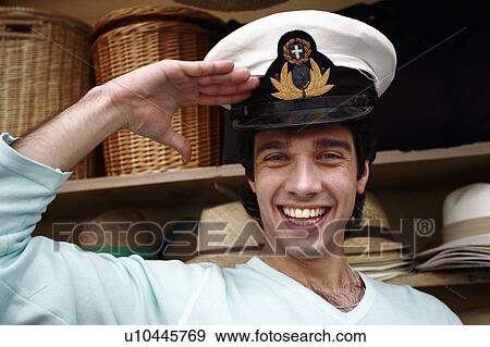 Stock Photo - Man trying on naval hat, saluting. Fotosearch