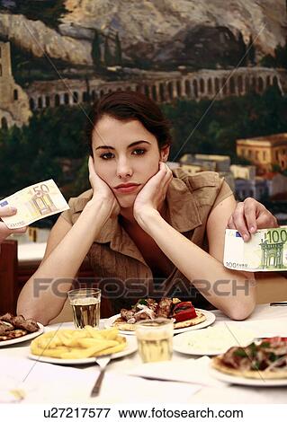 Stock Photo - Woman sulking at restaurant table with Euro bills. Fotosearch