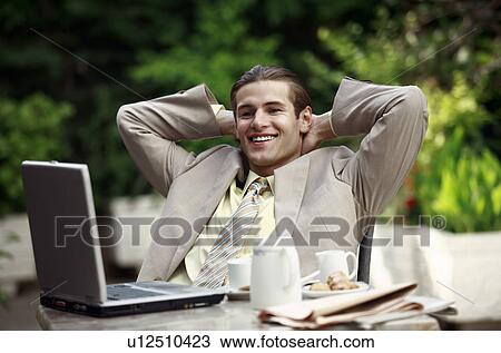 Stock Image - Businessman in garden cafe with laptop. Fotosearch