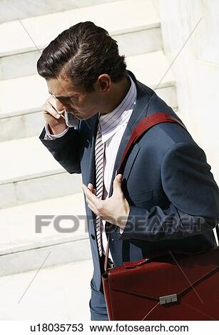 Stock Image - Businessman on the go on cell phone with briefcase. Fotosearch