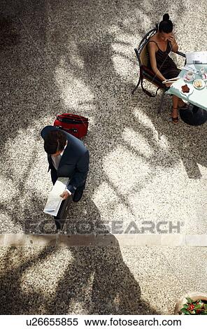 Businesswoman at cafe table, businessman walking by with suitcase View Large Photo Image Stock Photography - Businesswoman at cafe table, businessman walking by with suitcase. Fotosearch