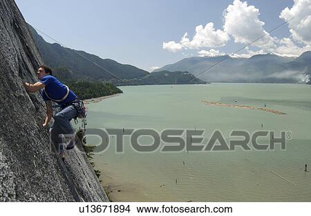 Man (20-25) climbing a rock face above the ocean, Squamish, B. C. View Large Photo Image Picture - Man (20-25) climbing a rock face above the ocean, Squamish, B. C.. Fotosearch