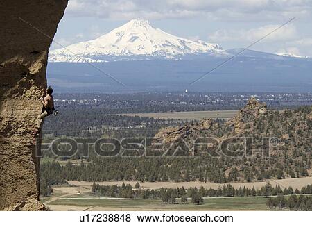 Stock Photo - Man (25-30) rock climbing with Mountain in background, Smith Rock State Park, Oregon, USA. Fotosearch