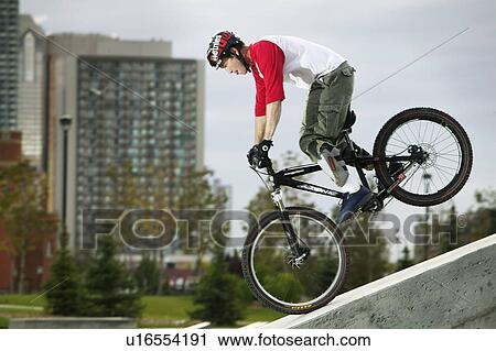 Stock Image - Profile of youth on mountain bike, city tower in background, Alberta, Calgary, Shaw Millenium Park. Fotosearch