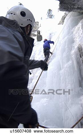 Stock Photo - Two Men (20-25) Ice climbing. One climber belays the other as a safety measure. Canmore, Alberta, Canada. Fotosearch