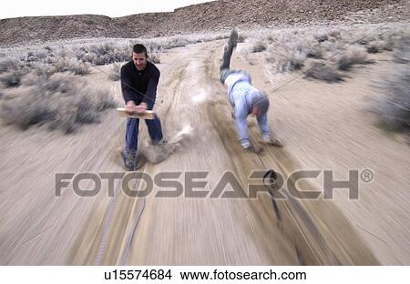 Two men (20-30) surfing behind a car on a dirt road, Bishop, California, USA View Large Photo Image Picture - Two men (20-30) surfing behind a car on a dirt road, Bishop, California, USA. Fotosearch