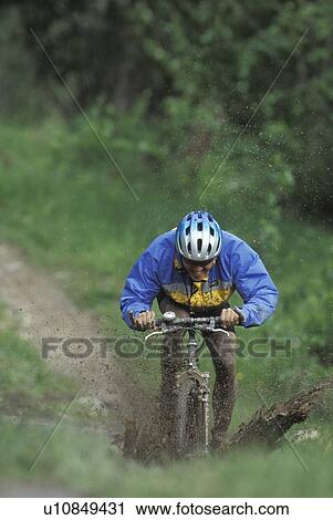 Stock Image - young man mountain biking through mud near Fernie, BC, Canada. Fotosearch