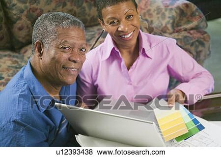Stock Photo - African American couple with paint swatches, laptop and building plans, B. C.. Fotosearch