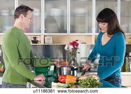 Stock Image - Couple cutting vegetables, with green kitchen compost pail for collecting kitchen scraps, Winnipeg, Canada. Fotosearch