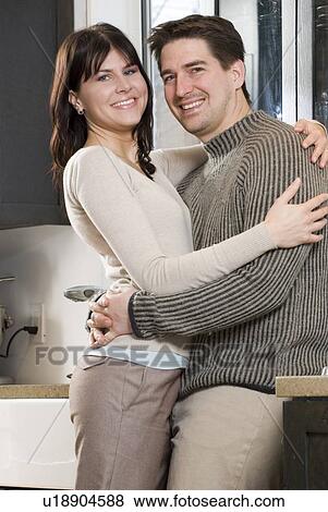 Couple embrace in kitchen. Home has recovered/recycled cupboards and hardwood floors, Winnipeg, Canada View Large Photo Image Stock Photo - Couple embrace in kitchen. Home has recovered/recycled cupboards and hardwood floors, Winnipeg, Canada. Fotosearch