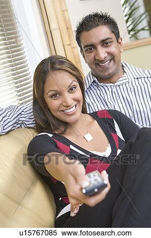Couple embracing on sofa with remote control, Winnipeg, Canada. Couple appear to be of Indian ethnicity. View Large Photo Image Stock Photography - Couple embracing on sofa with remote control, Winnipeg, Canada. Couple appear to be of Indian ethnicity.. Fotosearch