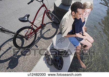 Stock Image - Young Couple rest from riding bikes at a fountain, shot from above, Vancouver, British Columbia. Fotosearch