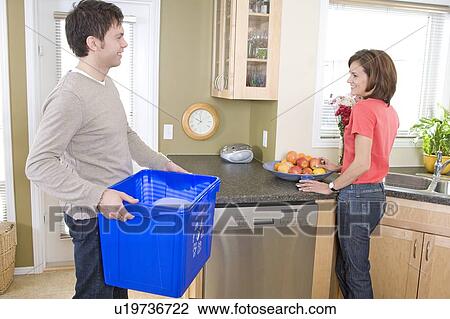 Stock Image - Couple in kitchen, man holding recyling bin, Winnipeg, Canada. Fotosearch