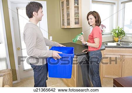 Stock Image - Couple in kitchen, woman putting plastic bottle into recyling bin, Winnipeg, Canada. Fotosearch