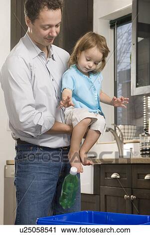 Stock Image - Man helping child drop plastic bottle into recycling bin, Winnipeg, Canada. Fotosearch
