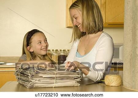 Stock Image - Mother and daughter tying up newspaper for recycling. Fotosearch