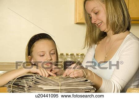 Stock Photography - Mother and daughter tying up newspaper for recycling. Fotosearch