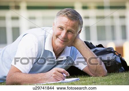Adult student lying on lawn of school with notebook View Large Photo Image Picture - Adult student lying on lawn of school with notebook. Fotosearch