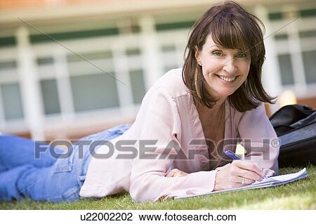 Stock Image - Adult student lying on lawn of school with notebook. Fotosearch