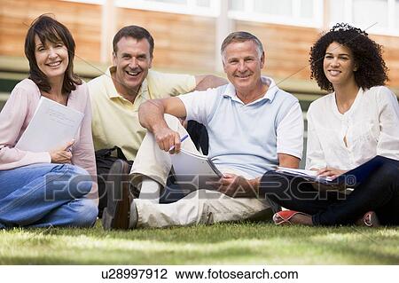 Stock Image - Adult students on lawn of school with notebooks. Fotosearch