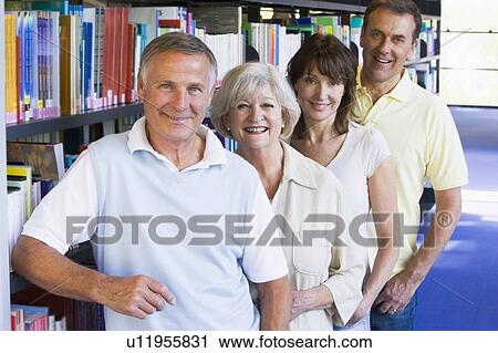 Stock Image - Four people in library standing by bookshelves. Fotosearch