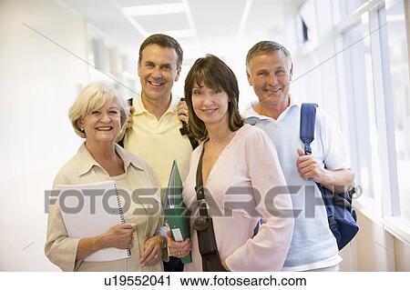Stock Image - Four people standing in corridor with books (high key). Fotosearch