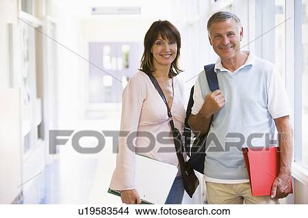 Picture - Man and woman standing in corridor with books (high key). Fotosearch