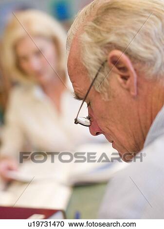 Stock Image - Man in library reading with woman in background (selective focus). Fotosearch
