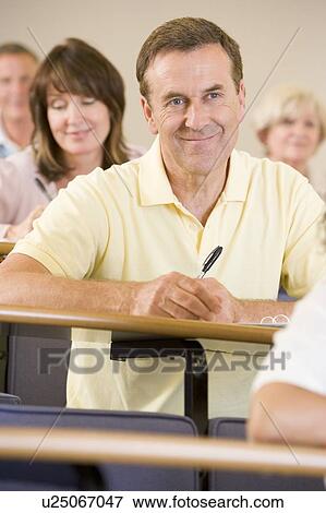 Stock Photo - Man sitting in adult classroom with students in background (selective focus). Fotosearch