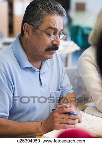 Stock Photo - Man sitting near woman in library with books and notepads (selective focus). Fotosearch