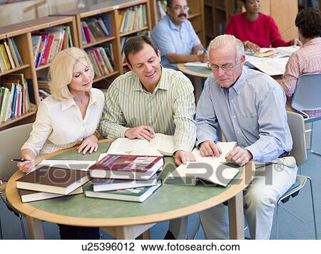 Stock Image - Three people in library with notepads (selective focus). Fotosearch
