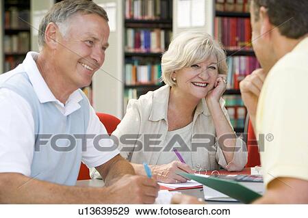 Stock Photo - Three people in library writing in notebooks (selective focus). Fotosearch
