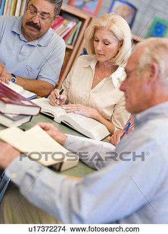 Three people sitting in library with books and notepads (selective focus) View Large Photo Image Picture - Three people sitting in library with books and notepads (selective focus). Fotosearch