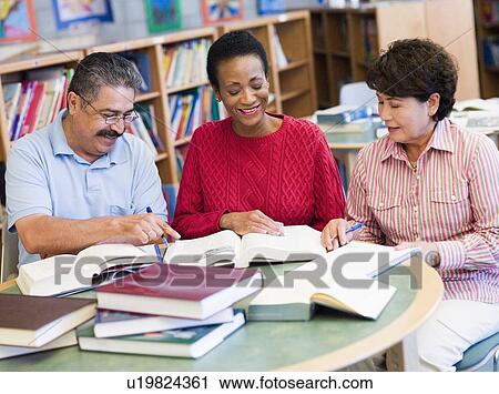 Stock Image - Three people sitting in library with books and notepads (selective focus). Fotosearch