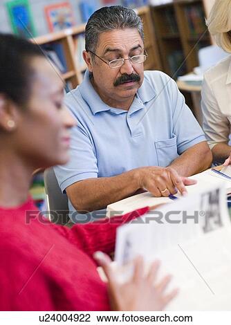 Stock Image - Three people sitting in library with books and notepads (selective focus). Fotosearch