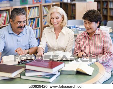 Stock Image - Three people sitting in library with books and notepads (selective focus). Fotosearch