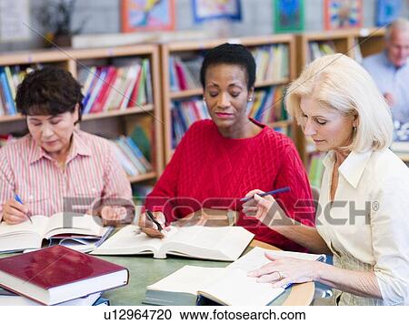 Stock Image - Three women sitting in library with books and notepads (selective focus). Fotosearch