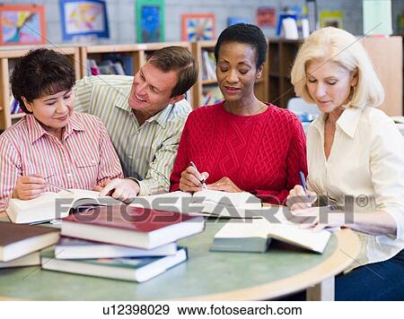 Stock Photo - Three women sitting in library with books and notepads while a man leans over them (selective focus). Fotosearch