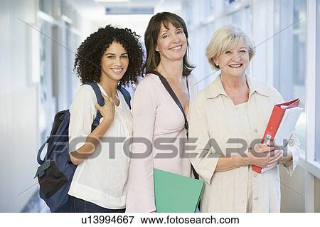 Stock Photo - Three women standing in corridor with books (high key). Fotosearch