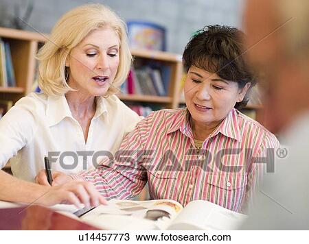 Stock Image - Two women sitting in library near a man with a book and notepad (selective focus). Fotosearch