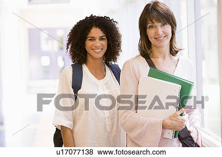 Two women standing in corridor with books (high key) View Large Photo Image Stock Photo - Two women standing in corridor with books (high key). Fotosearch