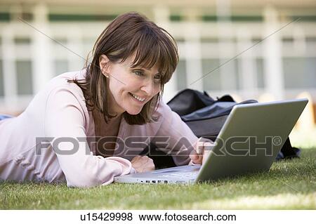 Stock Photo - Woman lying on lawn of school with laptop. Fotosearch