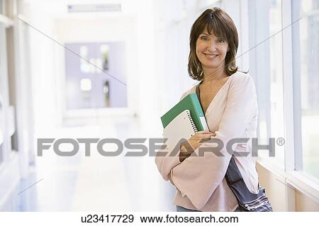 Stock Photo - Woman standing in corridor with books (high key). Fotosearch