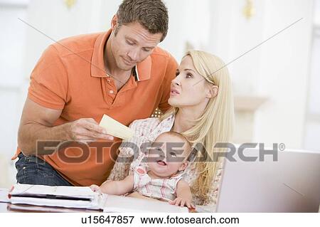 Couple and baby in dining room with laptop and paperwork View Large Photo Image Stock Photo - Couple and baby in dining room with laptop and paperwork. Fotosearch