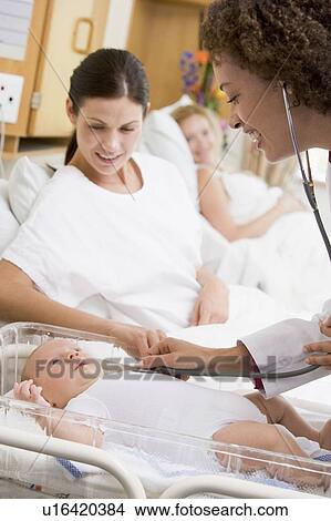 Picture - Doctor checking baby's heartbeat with new mother watching and smiling. Fotosearch