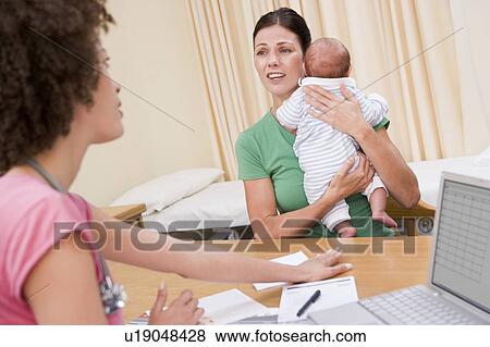 Stock Photo - Doctor with laptop and woman in doctor's office holding baby. Fotosearch