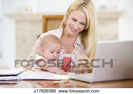 Stock Photo - Mother and baby in dining room with laptop smiling. Fotosearch